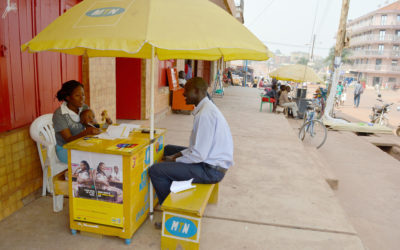 MTN female attendant attending to a black male customer seated on a yellow bench under an MTN umbrella