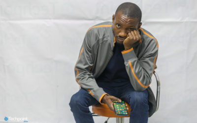 Image of a sad male model sitting on a swivel chair with a mobile phone in the left hand and the other hand under his chin