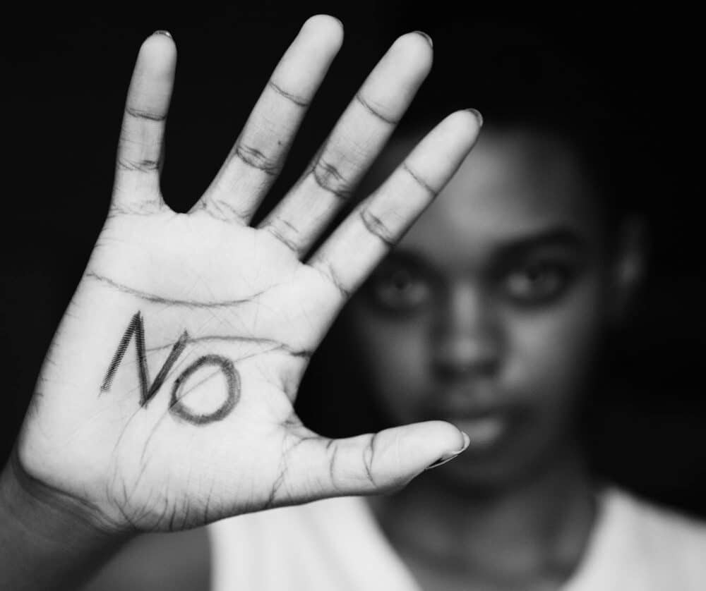 A woman raising her palms with the word NO written on it. This signifies advocacy for an end to gender based violence in the the world.