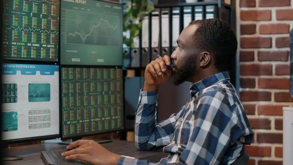 An African man looking at charts on multiple screens