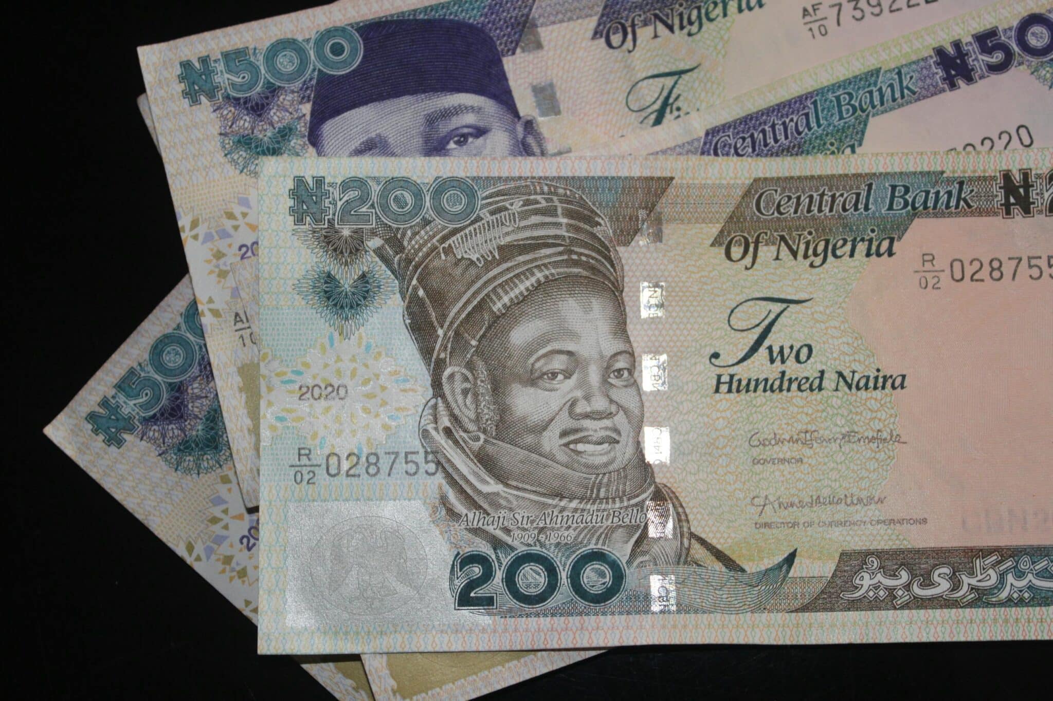 A close-up image of one old 200 naira note and two 500 naira notes on a plain balck background.