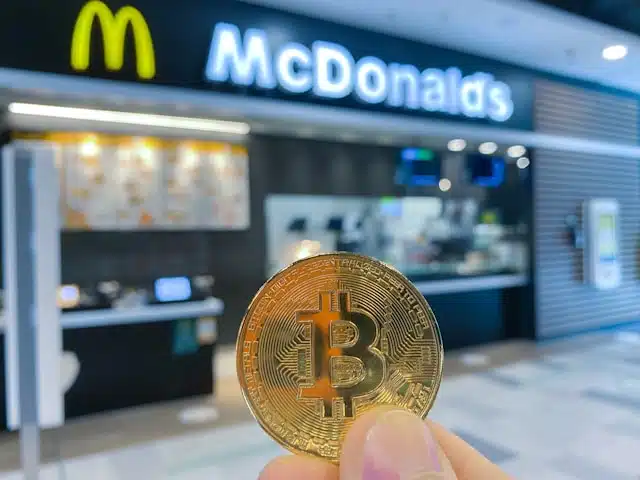 A picture of physical bitcoin coin with a McDonalds store in the background